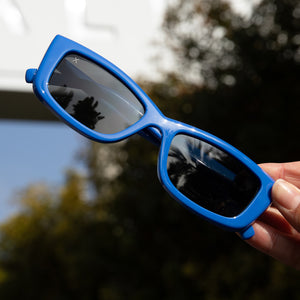 dime optics olympic sunglasses in poolhouse blue with grey lenses held up in the sun