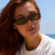 on model - female at the beach wearing dime optics featuring the agoura rectangular sunglasses with a black frame and grey lenses front view