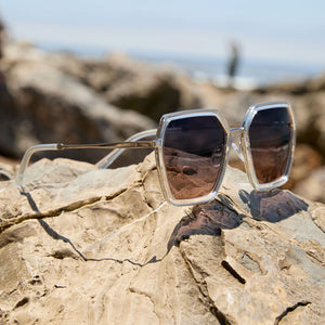 flat lay at the beach of dime optics featuring the alameda square sunglasses with a silver and crystal clear frame and orchid gradient lenses