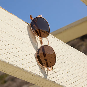flat lay of dime optics featuring the silverlake round sunglasses with a champagne gold frame and brown tint lenses front view