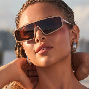 on model - nathalie paris wearing nathalie paris x dime optics mira shield sunglasses with a solid taupe frame and brown polarized lenses angled view